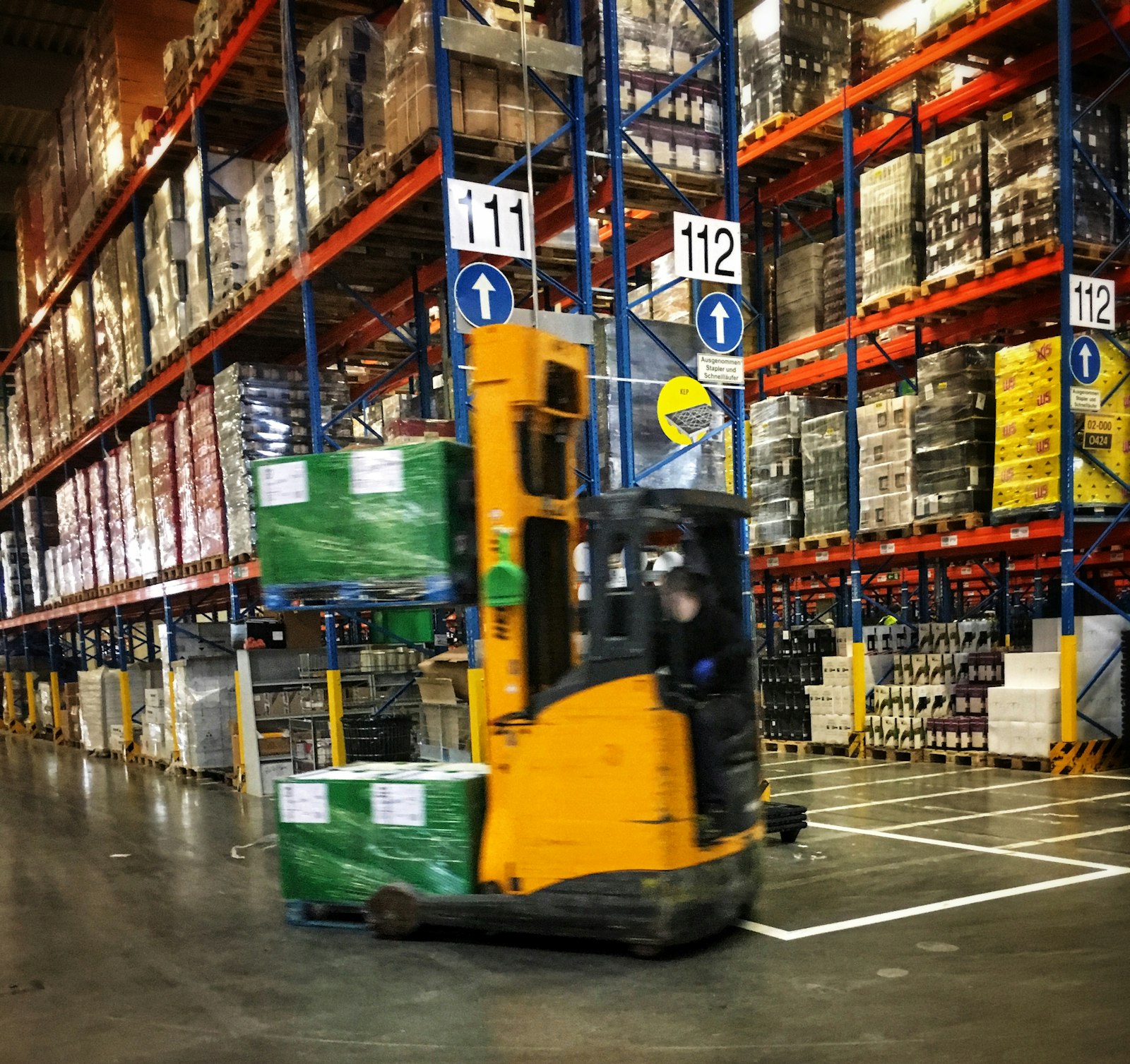 Operasional gudang logistik dengan forklift mengangkut pallet barang antar rak